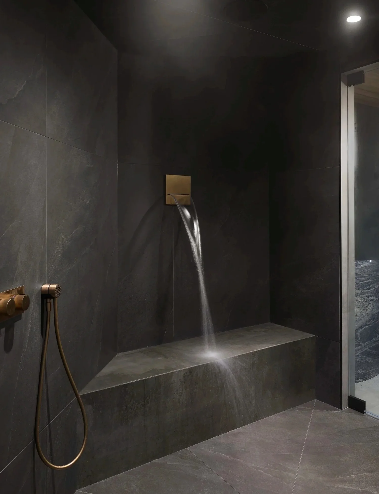 Dark slate shower with brass waterfall spout and built-in stone bench Toronto
